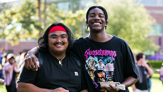 Two men holding bowls and smiling — the taller with his arm over the shoulder of the man next to him